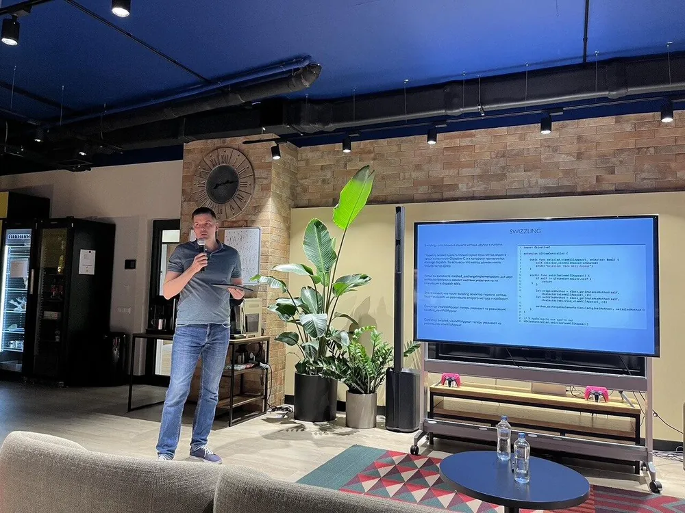 Aleksei Grebenkin speaking about method dispatch in Swift at the iOS meetup hosted by Garage IT in Tbilisi, with a slide on method swizzling on the screen behind him